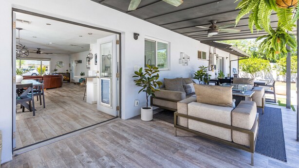 Ein großzügiger Wohnbereich mit einer Couch, Couchtisch und Topfpflanzen. Ein Deckenventilator und Blick auf den Garten sind vorhanden.