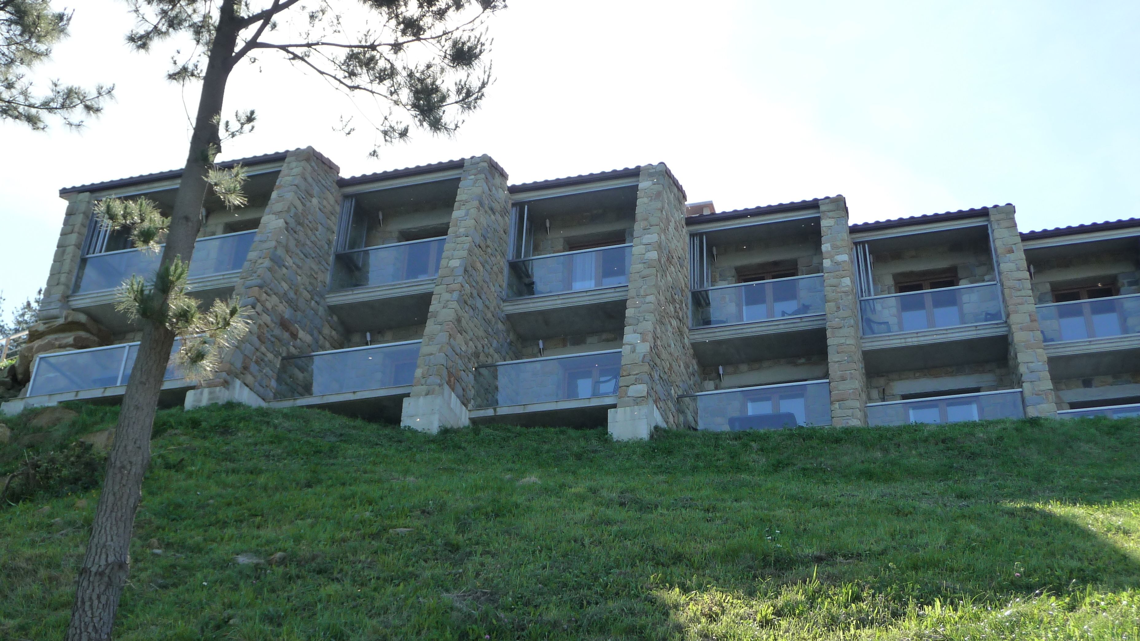 Um edifício de vários andares com varandas, fachada de pedra e um declive coberto de grama.