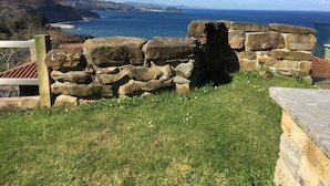Un mur de pierres bordé d’une zone herbeuse, d’où l’on peut admirer un paysage côtier avec des collines et une étendue d’eau.