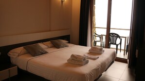 Une chambre d’hôtel avec un grand lit, deux oreillers, une table de chevet, une lampe fixée au mur et un balcon avec des chaises.