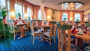 A restaurant with wooden tables and chairs, blue patterned carpet, and large windows with curtains. - Hotel Waldeck Garni (Kist)