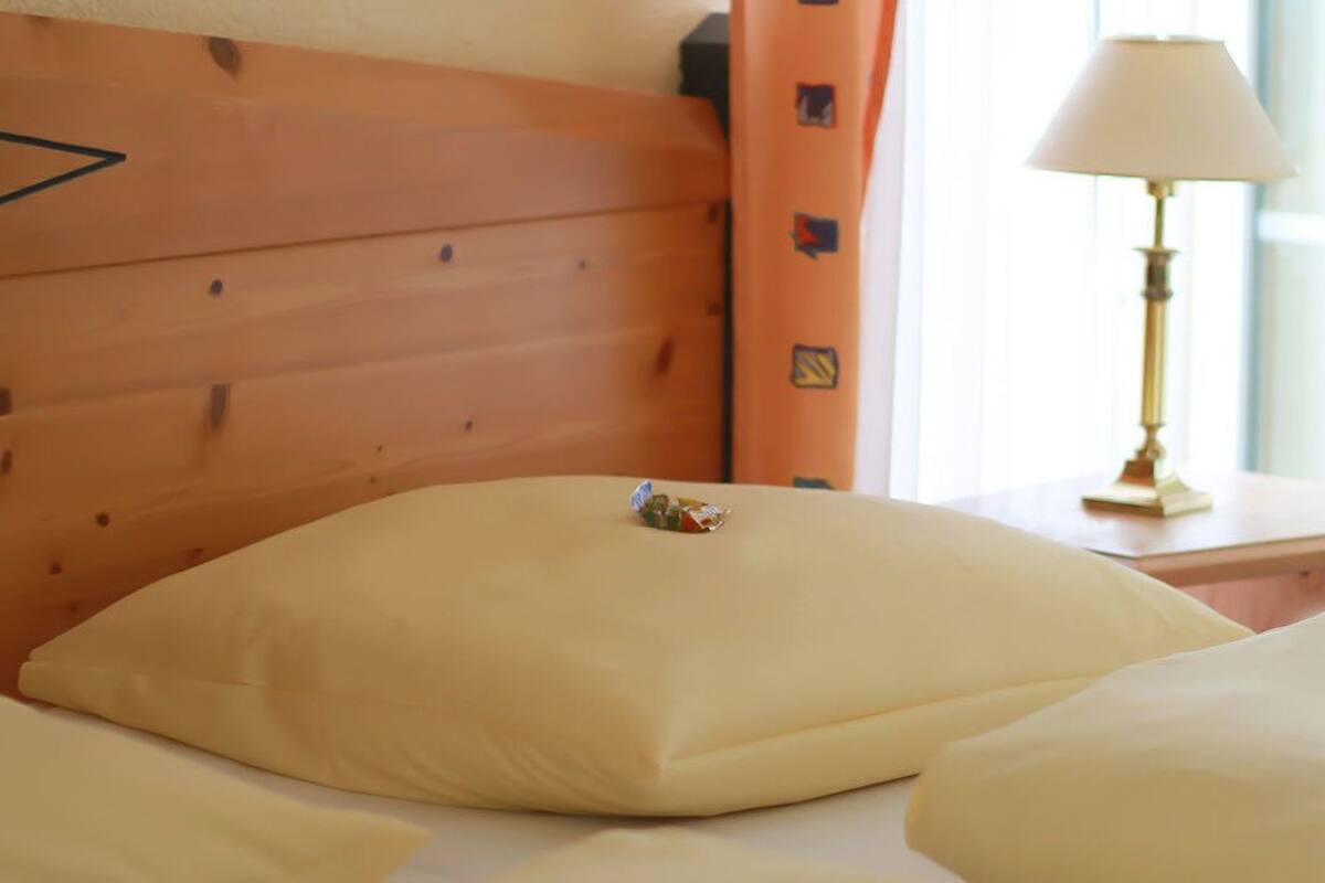 A hotel room with a wooden headboard, a bedside table with a lamp, and a pillow on the bed.