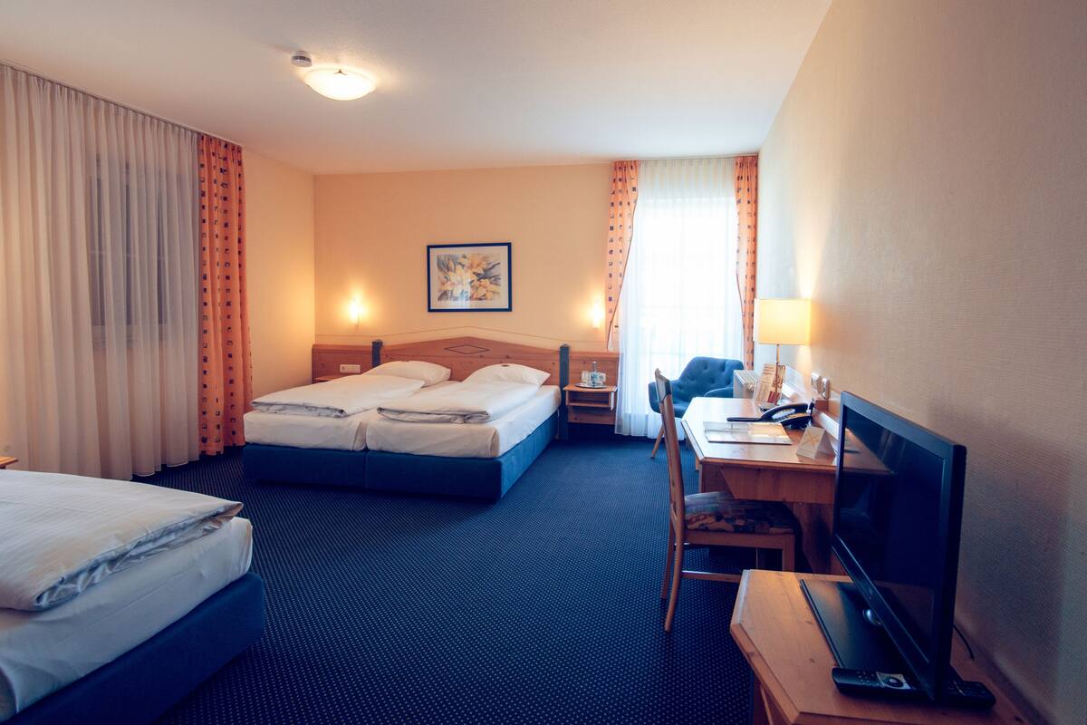 A hotel room with two beds, a desk with a computer and phone, a chair, and a TV.