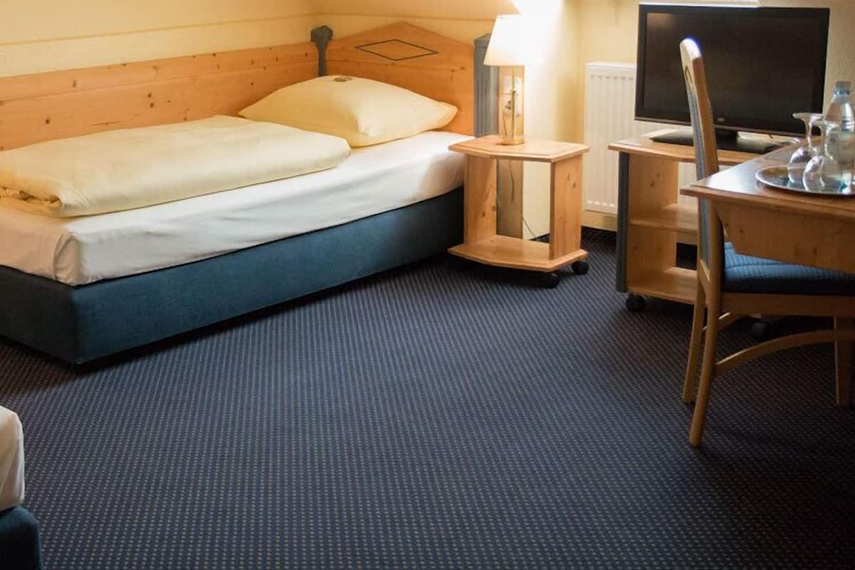 A hotel room with a bed, a desk with a chair, a lamp, and a television.