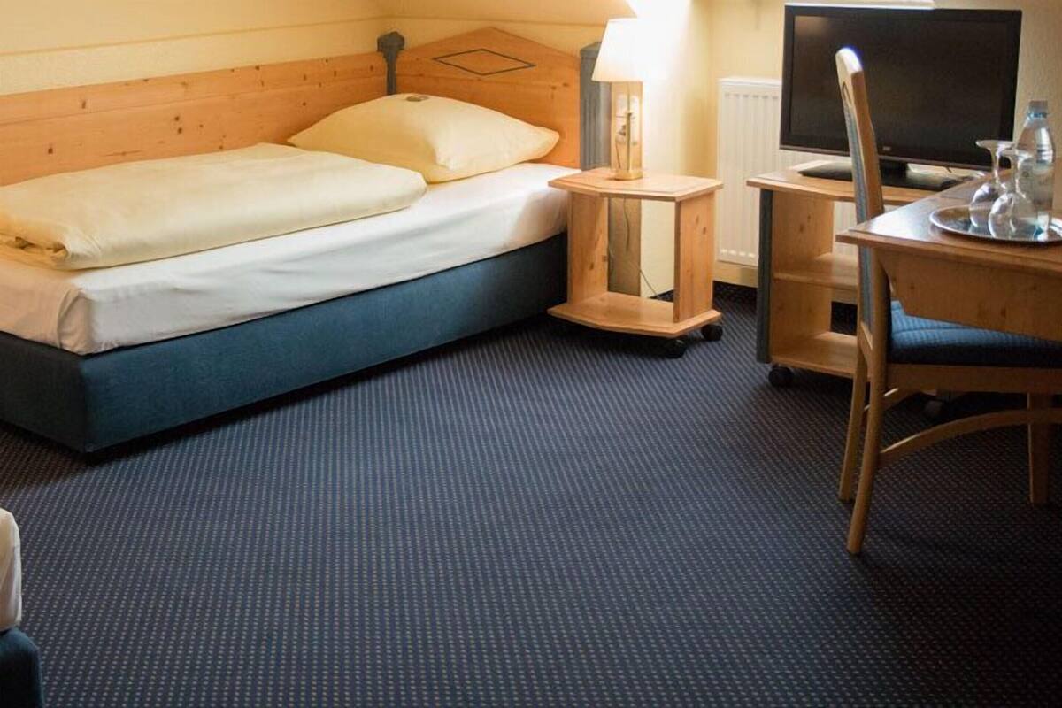 A hotel room with a bed, bedside tables, a desk with a chair, a lamp, and a television.