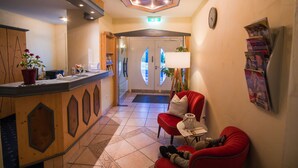 A hotel lobby with a reception desk, red seating area, and a clock on the wall. - Hotel Waldeck Garni (Kist)