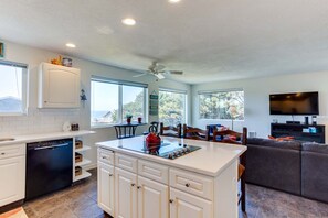 Enjoy a spacious kitchen with a central island, a cozy living area with a sofa and flat-screen TV, and large windows offering views of the surrounding landscape.