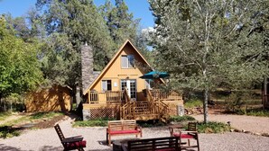 A lodge with a wooden deck, outdoor seating, and a stone chimney.