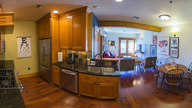 Una cocina con armarios de madera, un refrigerador de acero inoxidable, horno empotrado y una zona de comedor con una mesa redonda y sillas.
