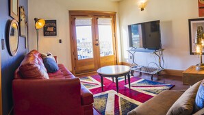 Una sala de estar acogedora con un sofá rojo, un sofá marrón, una mesita redonda y un televisor sobre un mueble.