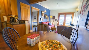 Un comedor con una mesa de madera, sillas y una pizza sobre una tabla de madera. Hay seis botellas de salsa en la mesa.