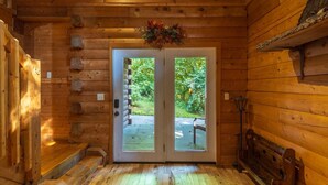 A log cabin interior with a wooden floor, a bench, a door leading outside, and a small table with a lamp. - *Veteran Owned, Wi-Fi, pet friendly, playground (Lancaster)
