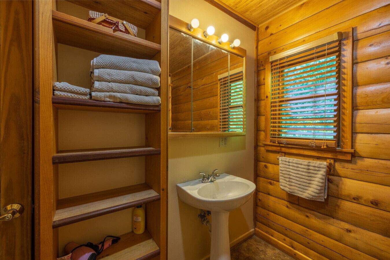 Un baño de cabaña de madera con lavamanos, espejo y repisas.