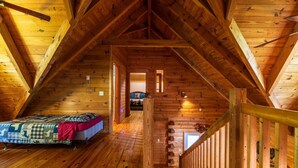 A wooden attic bedroom with a bed, a staircase, and a view into another room. - *Veteran Owned, Wi-Fi, pet friendly, playground (Lancaster)