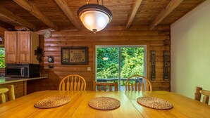 A wooden dining table with woven placemats, wooden chairs, a wooden ceiling, a kitchen area with a microwave, and a view of greenery through a window. - *Veteran Owned, Wi-Fi, pet friendly, playground (Lancaster)