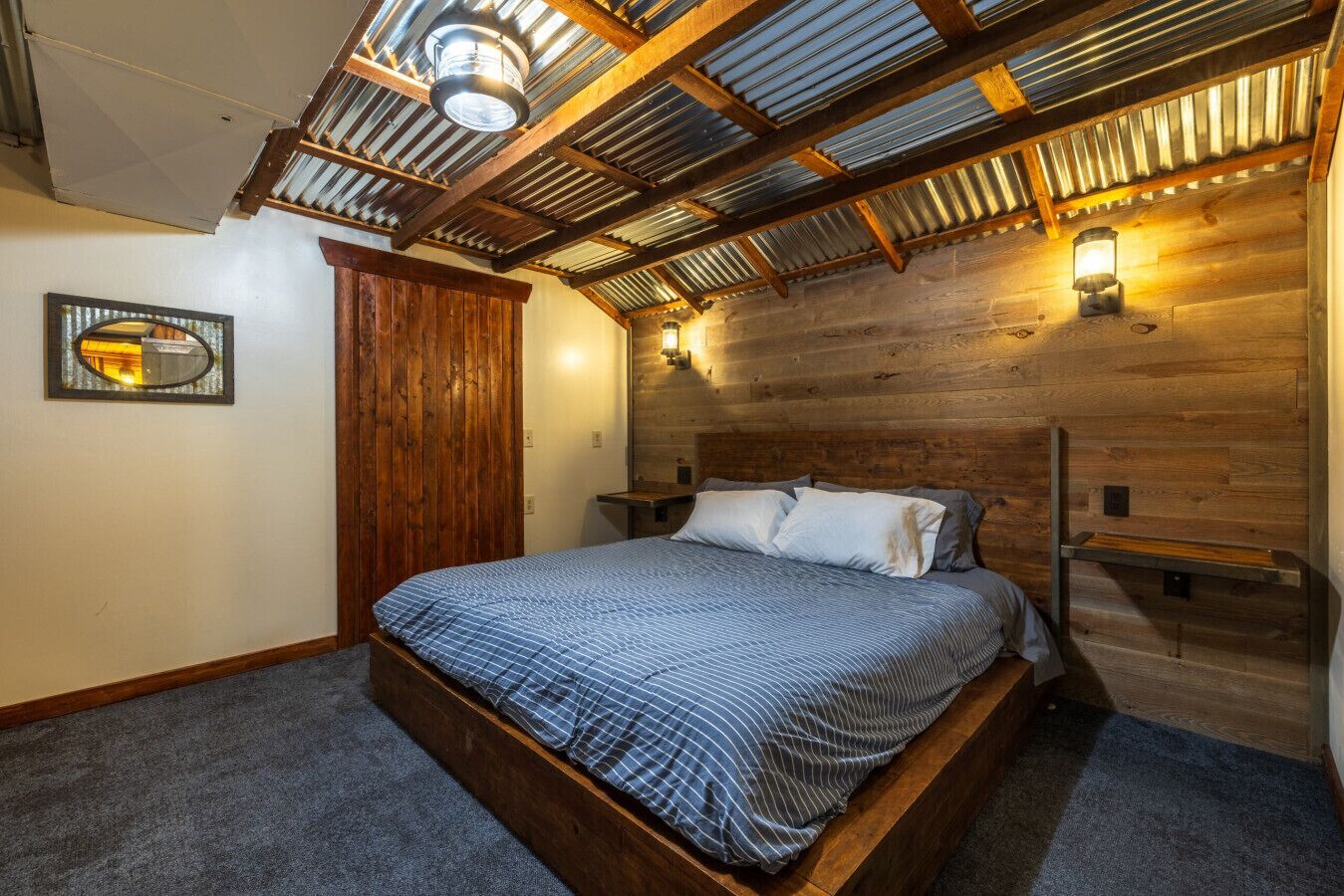 A bedroom with a wooden headboard, a bed with a blue striped bedspread, and a skylight above.