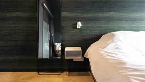 Une chambre à coucher moderne avec un grand miroir, une table de chevet avec une lampe et un lit soigneusement fait.