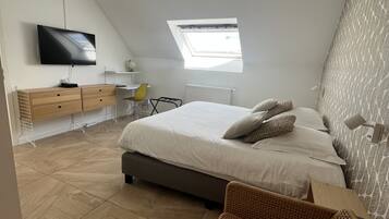 Een moderne slaapkamer met een schuine wand, een groot bed, een televisie, een bureau en een raam.