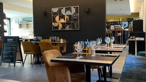 Un intérieur de restaurant moderne avec des tables en bois, des chaises rembourrées et une œuvre d’art centrale accrochée au mur.