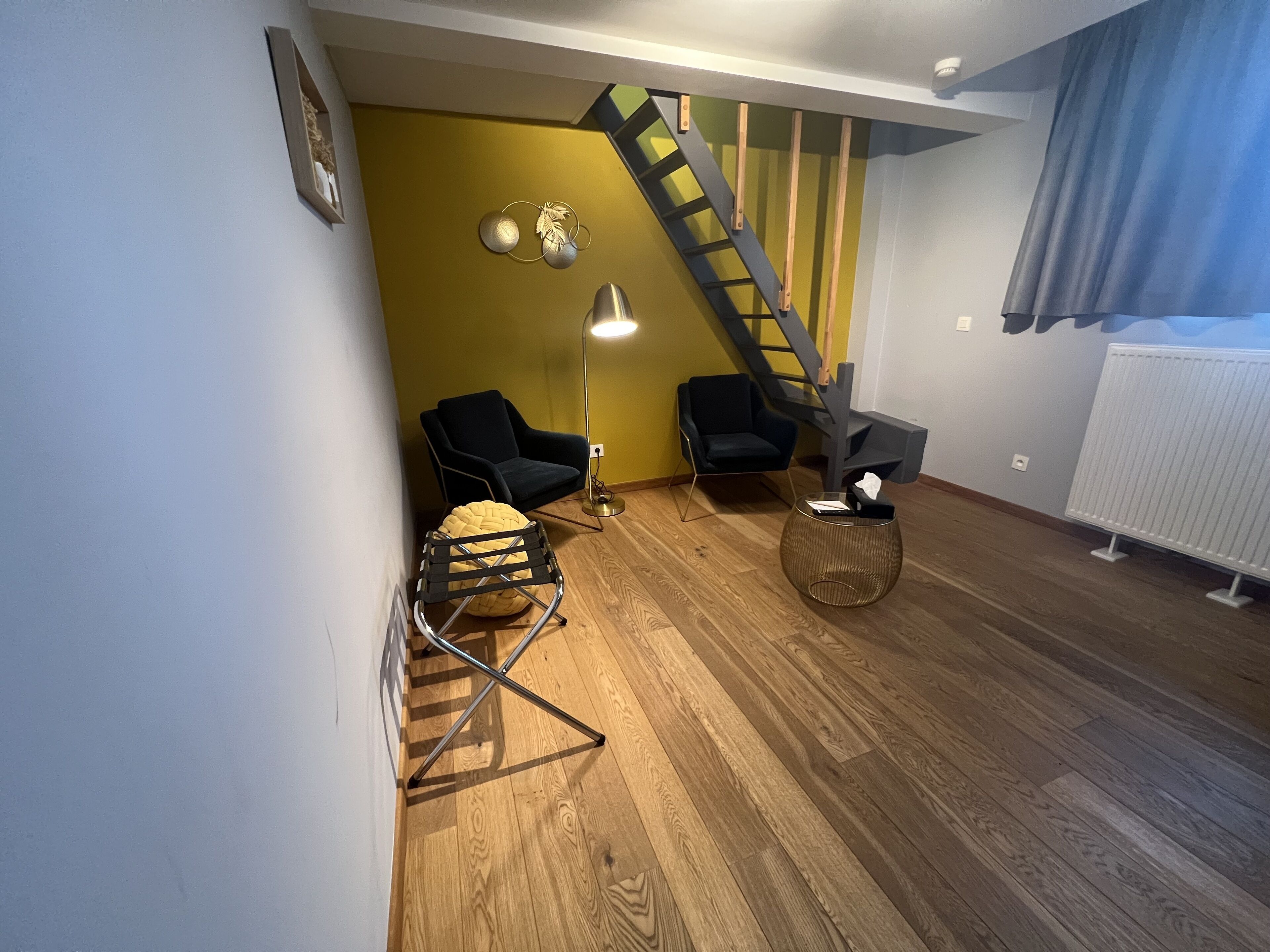 A modern living room with two black chairs, a floor lamp, a small round table, and a wooden staircase.