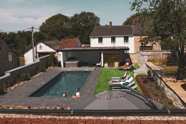 A swimming pool with a covered patio area, surrounded by stone walls and a grassy lawn. - Le Presbytère de Sautour (Philippeville)
