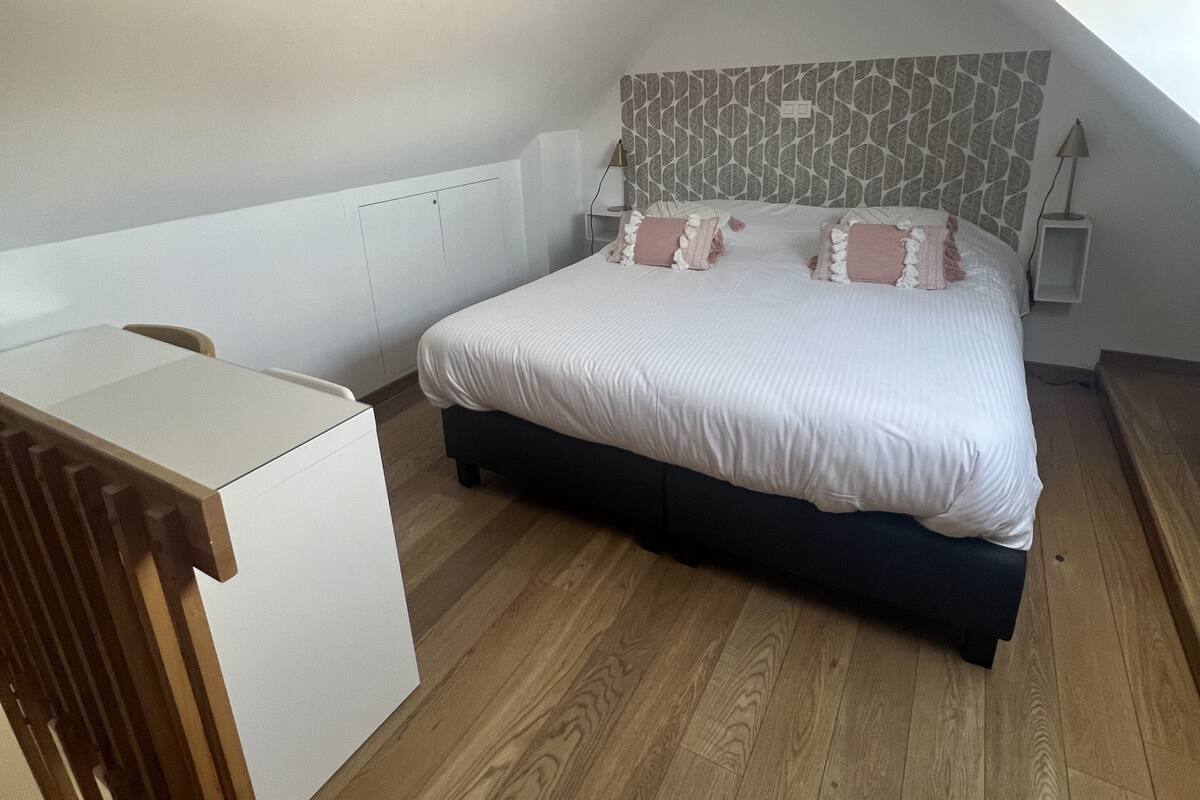 Une chambre avec un plafond en pente, un lit avec une literie blanche, une table de chevet et un plancher en bois.