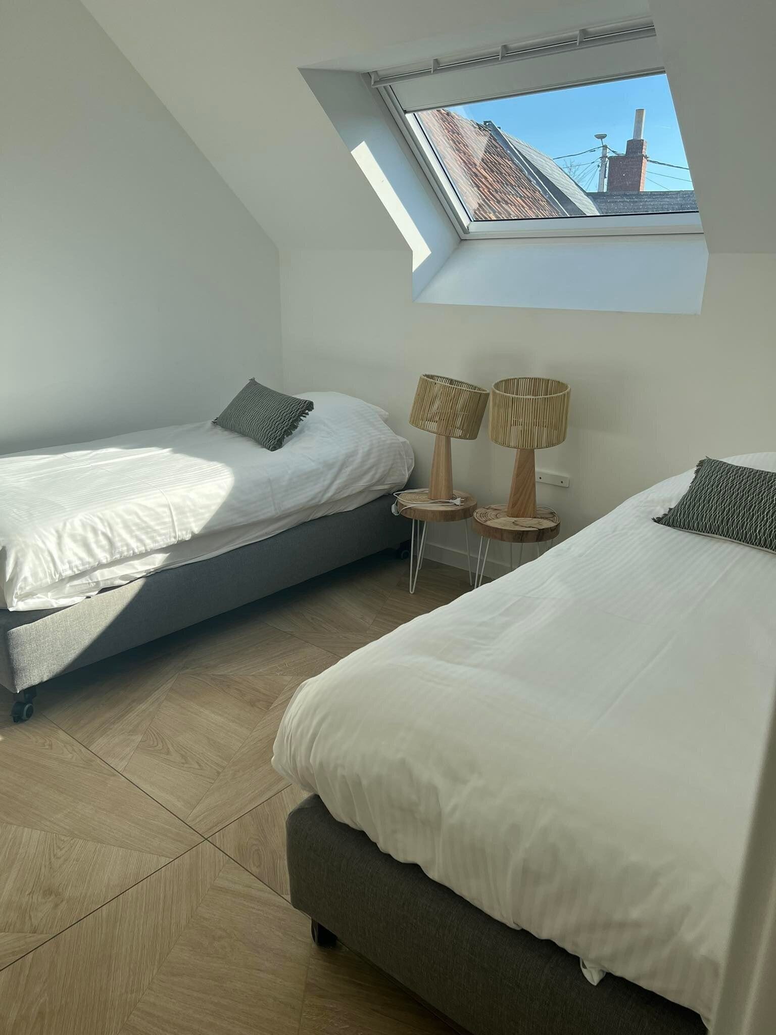 A bedroom with two beds, a skylight, and a view of buildings outside.