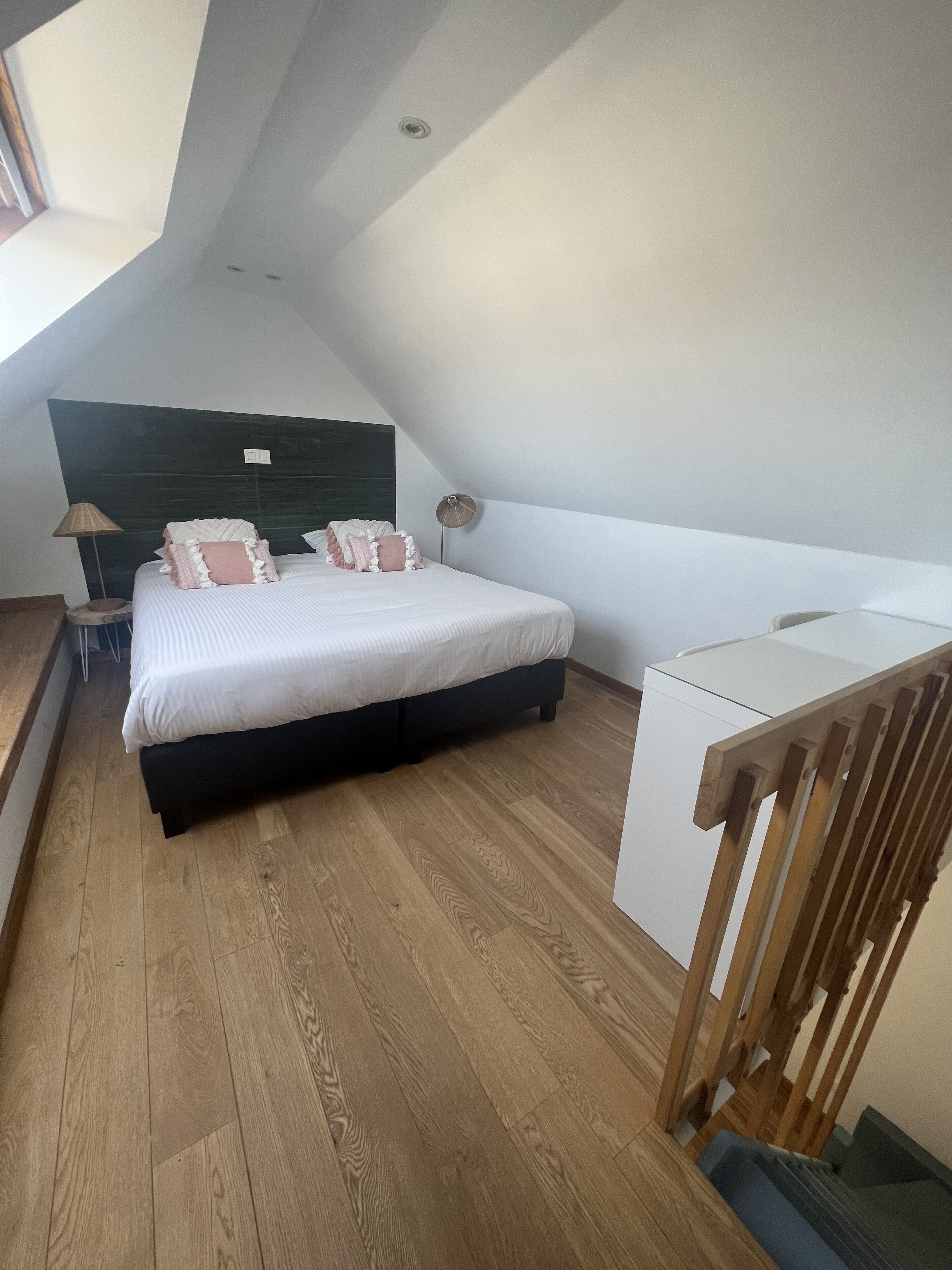 Een slaapkamer met een bed, nachtkastje, lamp en een bureau.