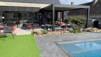 A modern outdoor patio with a pool, stone walls, and a covered seating area.