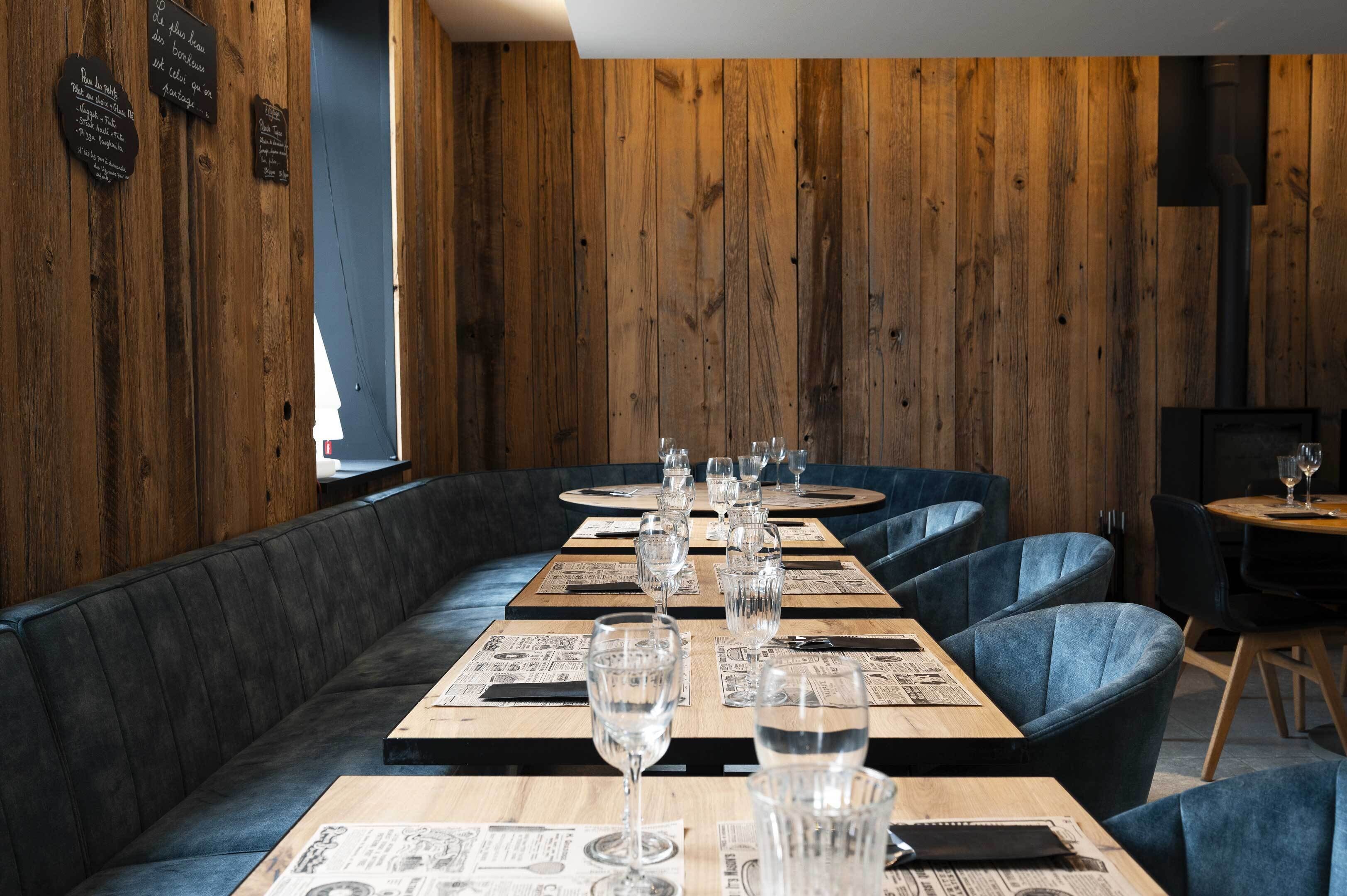 A restaurant with wooden walls, black leather booths, and tables set with glasses and menus.