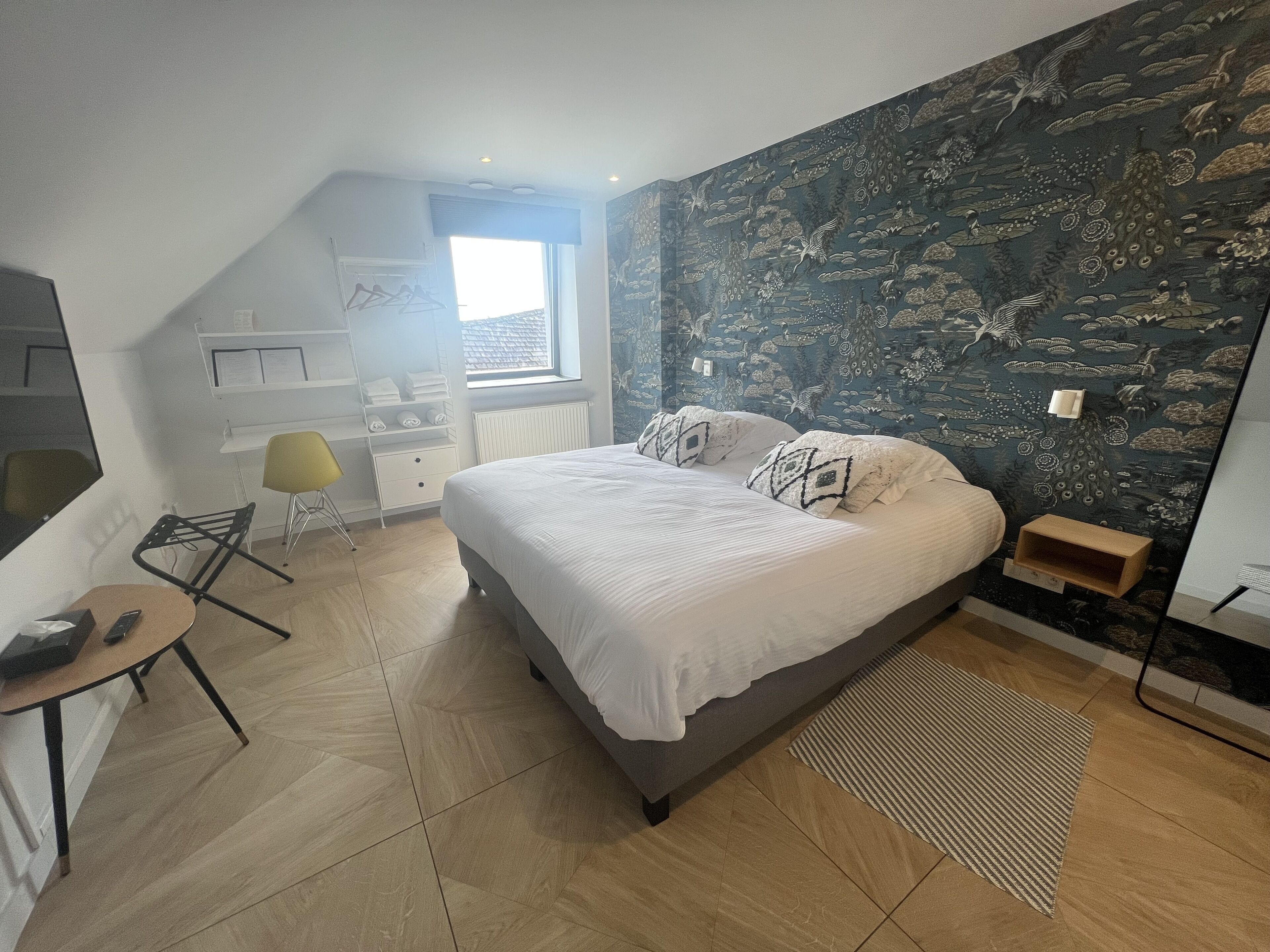 A bedroom with a bed, a desk, a chair, a radiator, and a window.