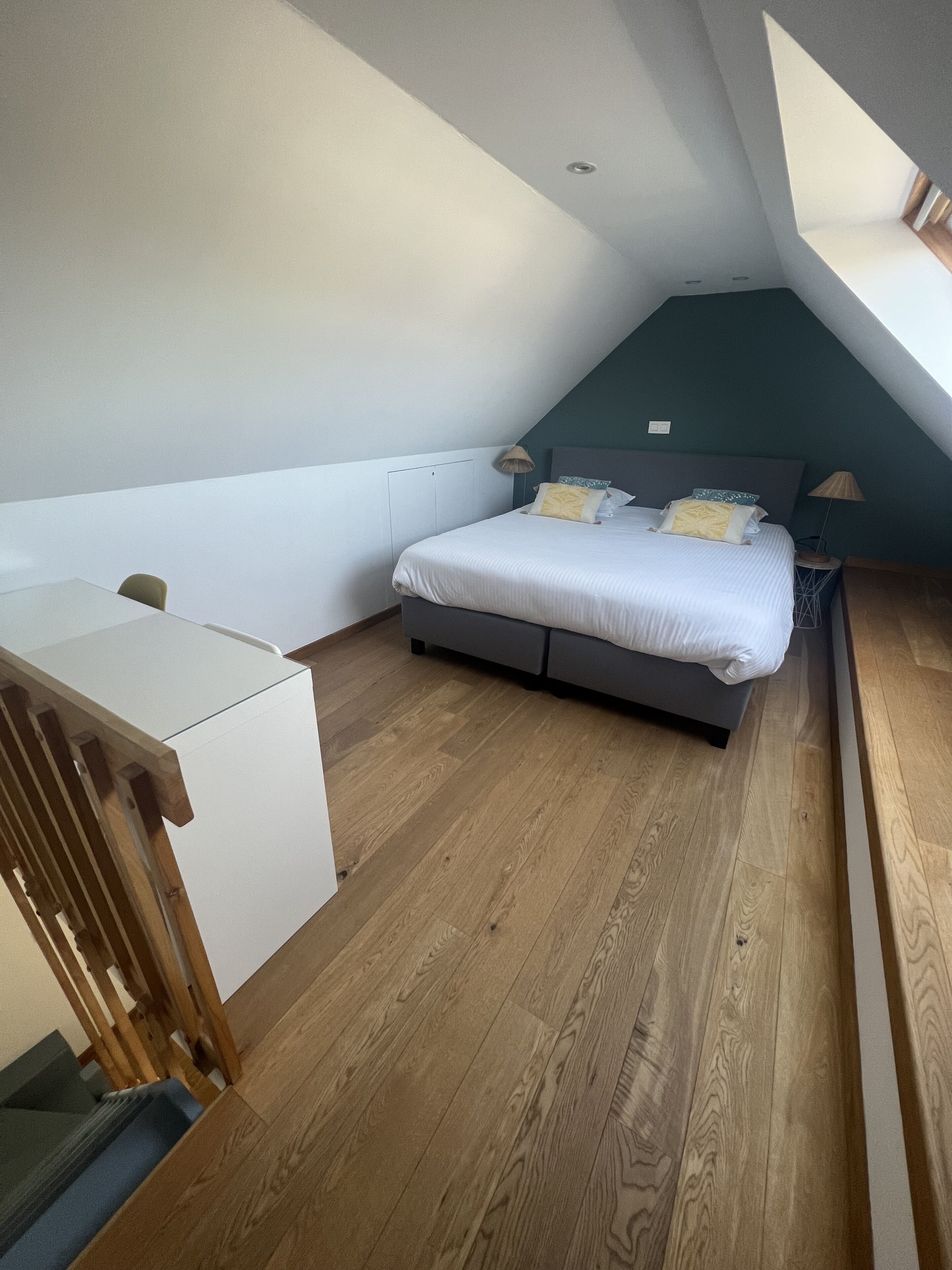 Ein Schlafzimmer mit Bett, Nachttischen, Schreibtisch und geneigter Decke.