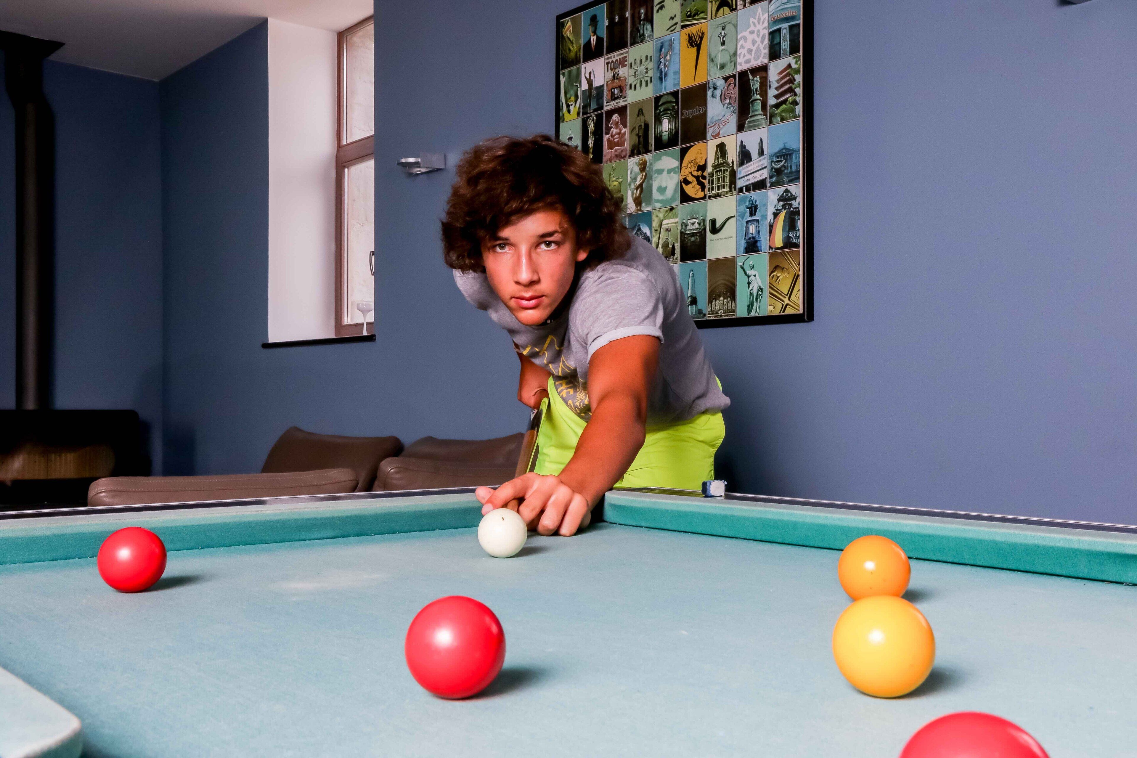 A person playing pool in a room with a blue wall and a framed collage of images.