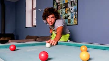 A person playing pool in a room with a blue wall and a framed collage of images.