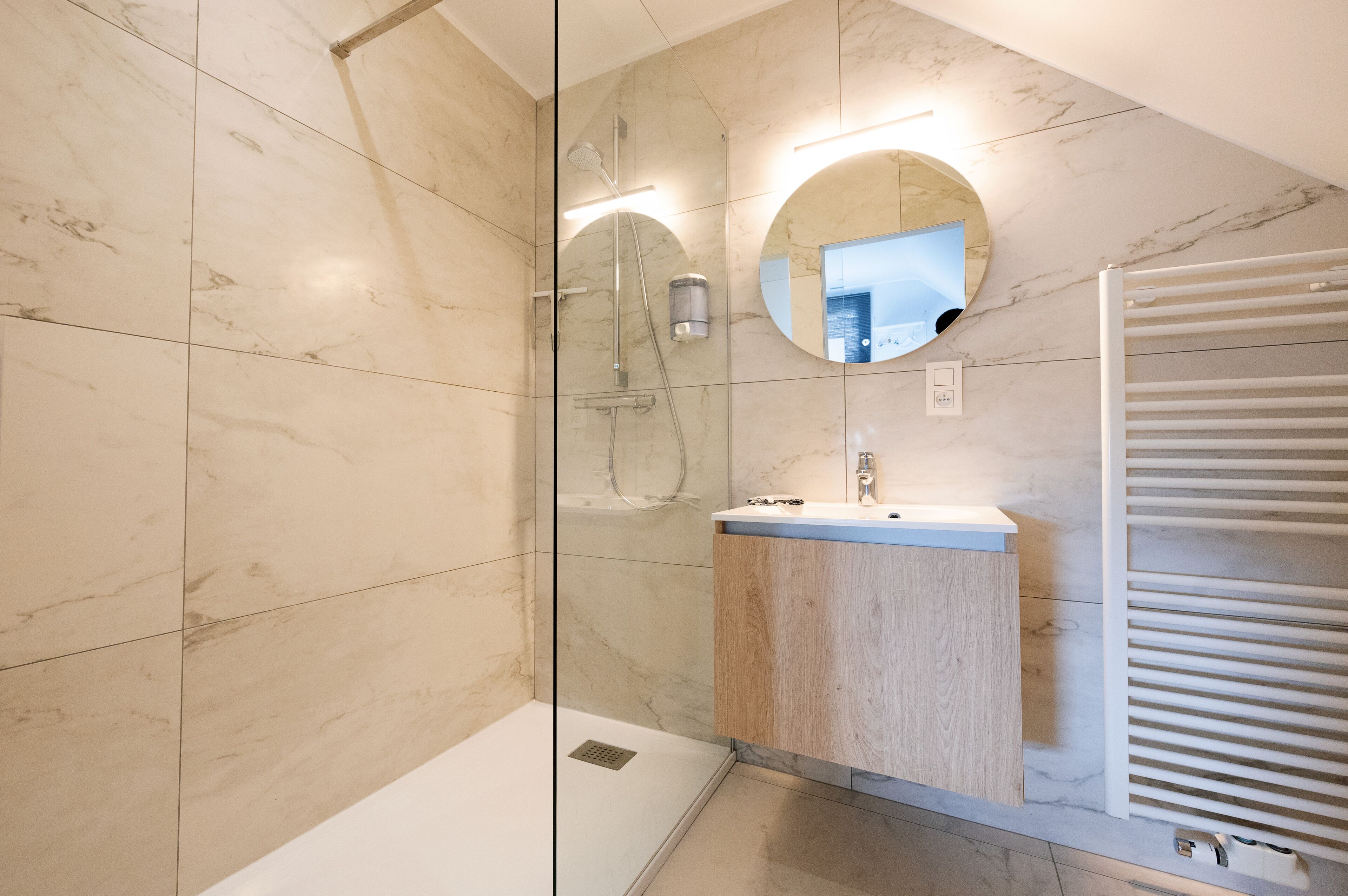 Un baño moderno con ducha envuelta en vidrio, tocador de madera con lavamanos y un perchero para toallas.