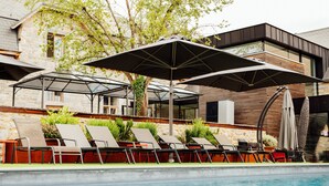 Un espace piscine agrémenté de chaises longues et de parasols, entouré de bâtiments en pierre et de verdure.