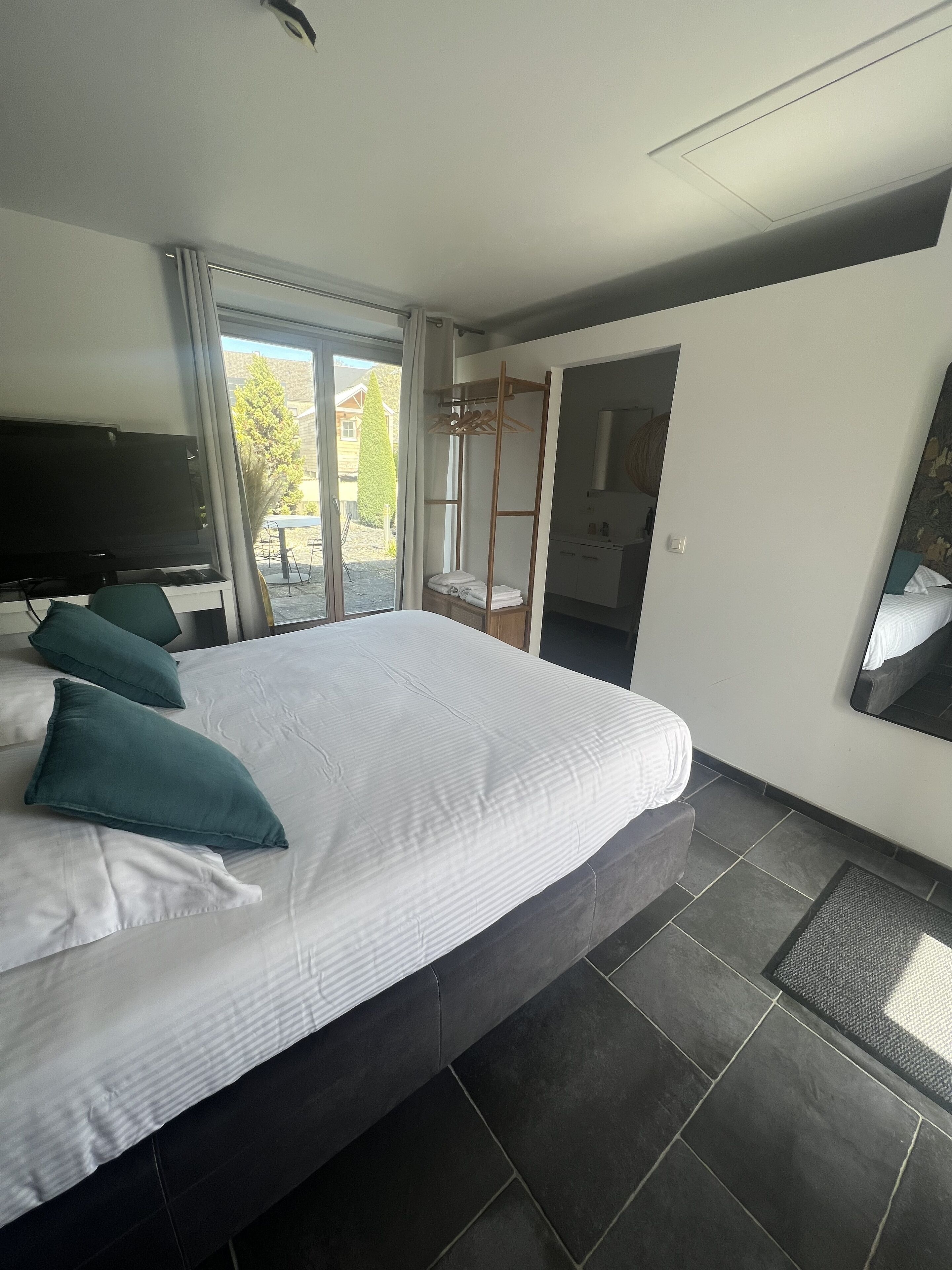A modern hotel room with a large bed, a flat-screen TV, a walk-in closet, and a view of the outdoors.