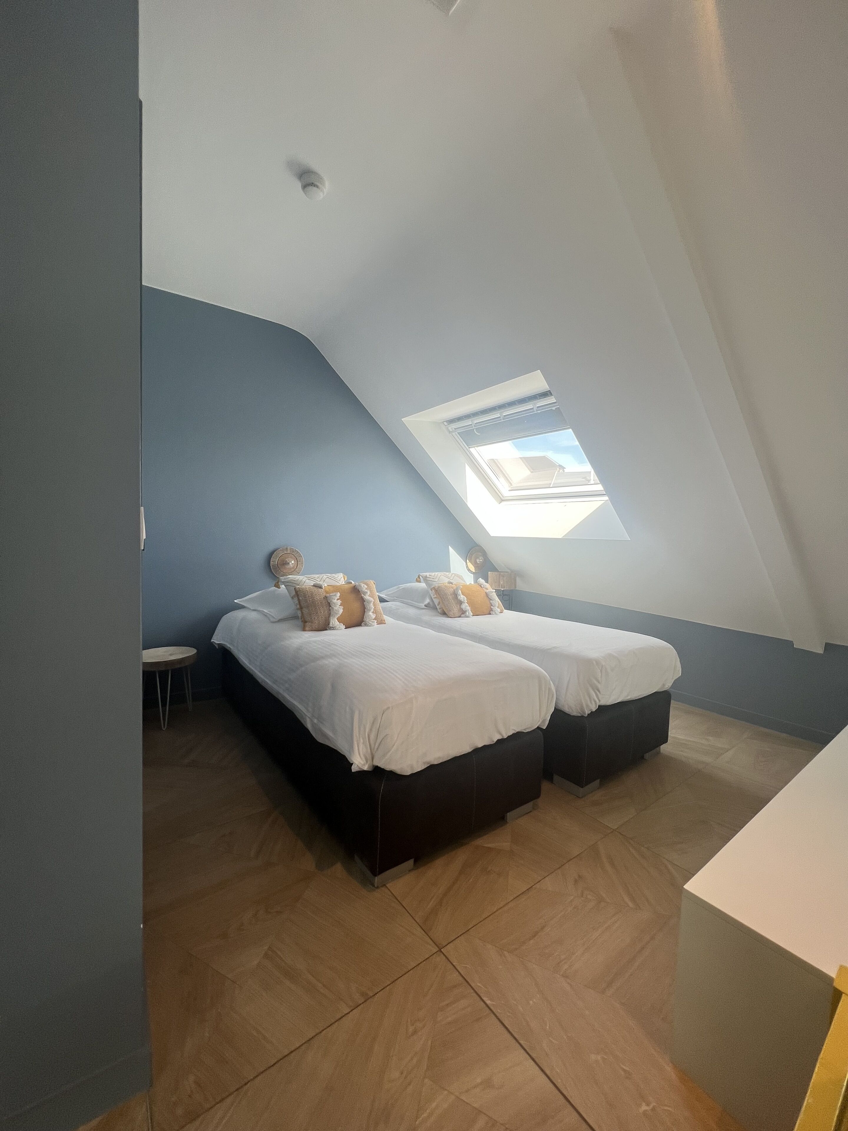 Una habitación con dos camas, un tragaluz y una pequeña mesa.
