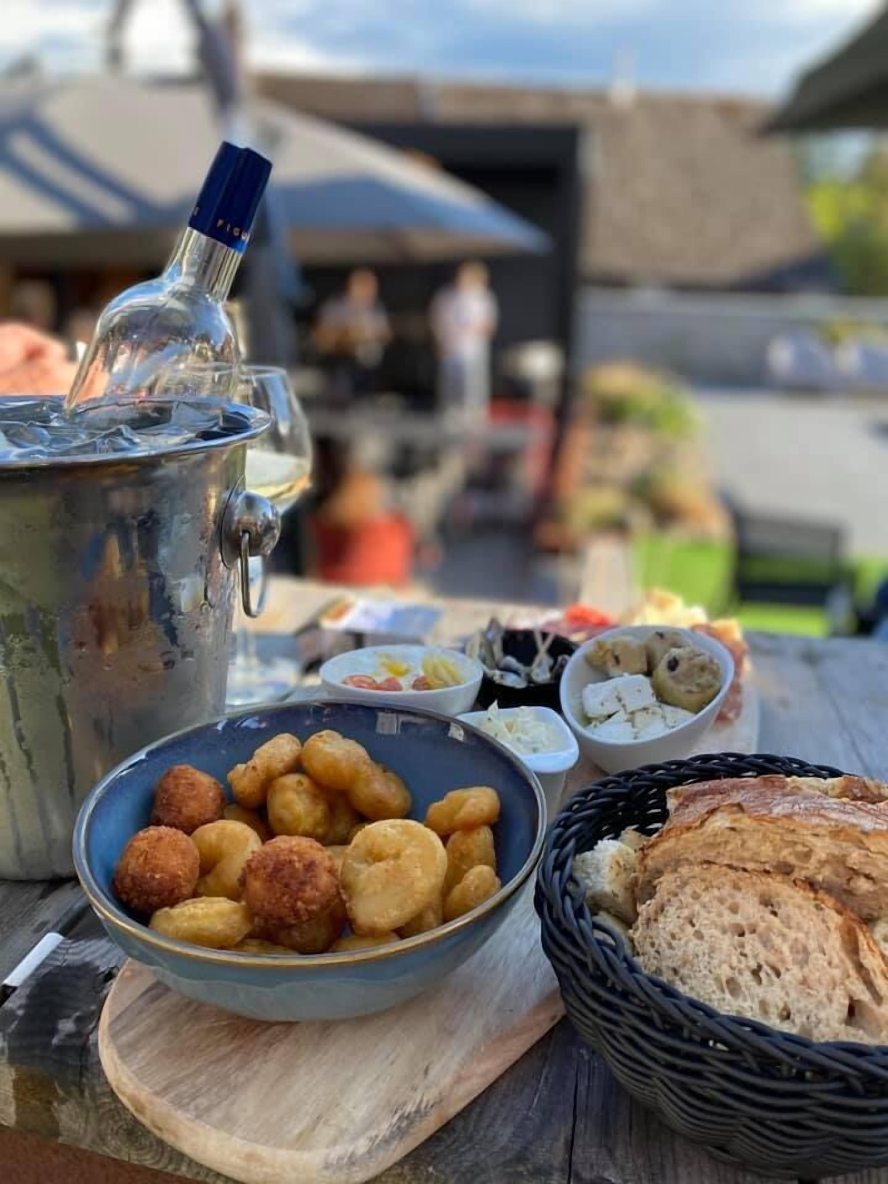 Une table avec un récipient en métal, un bol de collations frites, un panier de pain et divers petits plats.