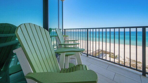 A balcony with green Adirondack chairs overlooking a beach.