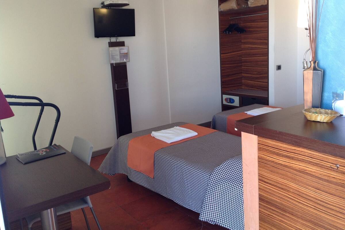 A hotel room with two beds, a desk, a television, and a wooden wardrobe.