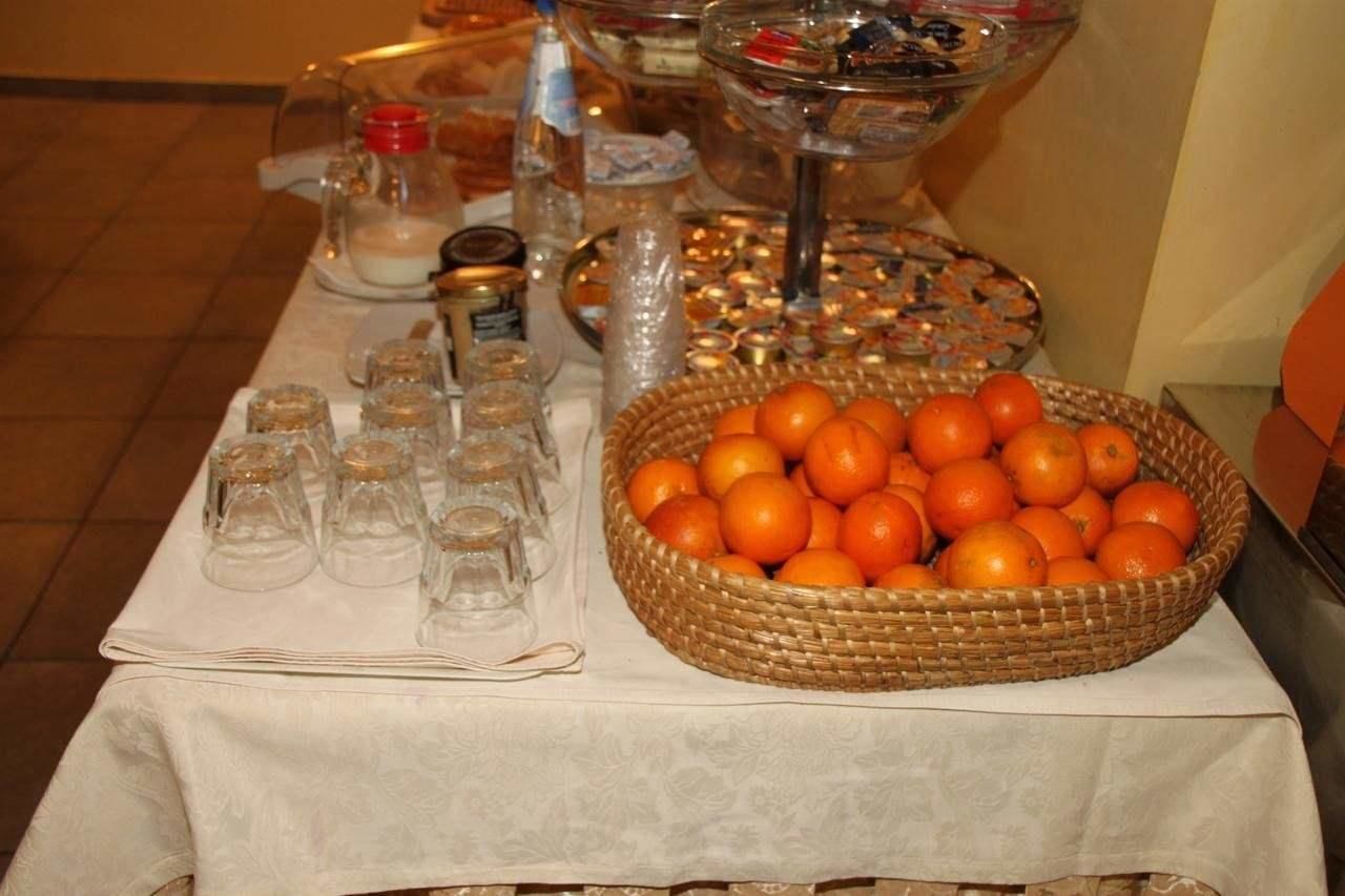 Une table de buffet avec un grand panier en osier rempli d’oranges, plusieurs petits récipients en verre et une variété d’aliments.