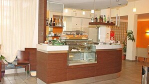 Un moderno vestíbulo de hotel con un mostrador de recepción curvo, una vitrina con pasteles y una zona de bar con botellas.