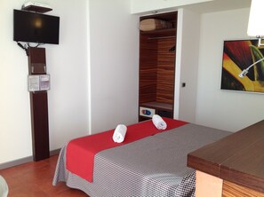 A hotel room with a massage table, a TV mounted on the wall, a wooden wardrobe, and a painting on the wall. - Hotel Bed & Business (San Giovanni Teatino)