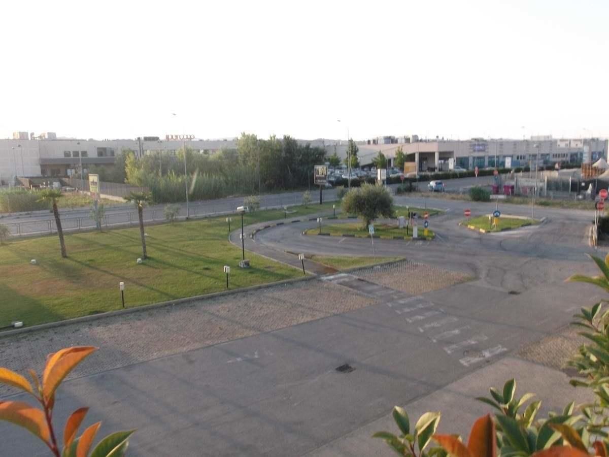 Un parcheggio con un'isola centrale, circondato da un'area verde e alberi.