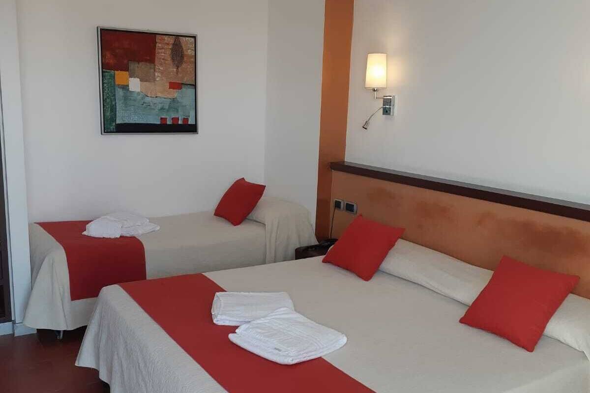A hotel room with two beds, red and white bedding, a painting on the wall, and a single light fixture.