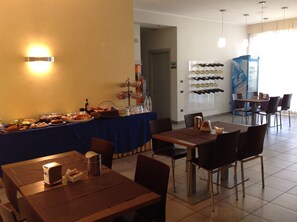 A dining area with tables and chairs, a buffet with various food items, and a wine rack with bottles. - Hotel Bed & Business (San Giovanni Teatino)