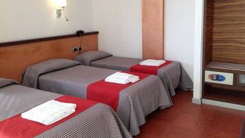 Ein Hotelzimmer mit drei Betten, jedes mit einer rot-schwarz karierten Tagesdecke und weißen Handtüchern. Es gibt ein hölzernes Kopfteil, eine an der Wand befestigte Lampe und einen Holzschrank mit darin befindlichen Kleidungsstücken.