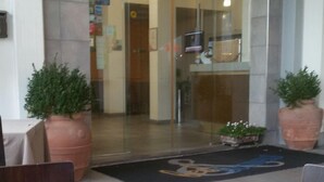 Zona de recepción de un hotel, con mostrador de recepción, plantas en macetas y una mesa con un croissant y café.