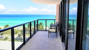 A balcony with a view of the ocean, a table, and two chairs. - Beautiful Direct Oceanfront 4 Bedroom with Blue Ocean Views - 702 (Miami Beach)